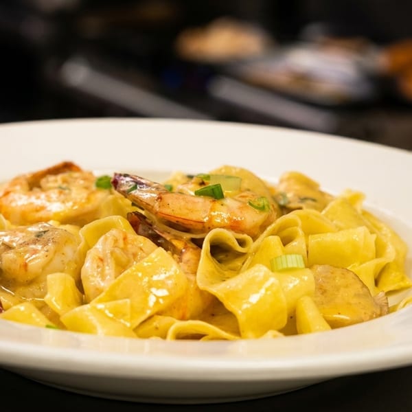 Close-up of shrimp and pasta in a creamy sauce, garnished with green onions, in a white bowl.