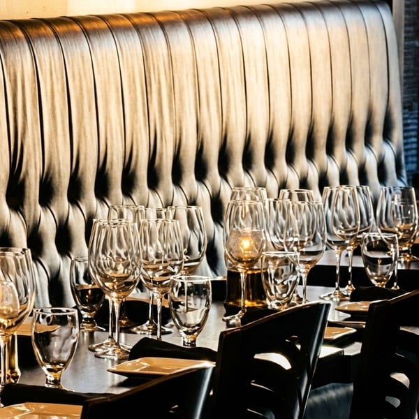 Elegantly set dining table with wine glasses, plates, and candles, against a tufted leather booth.