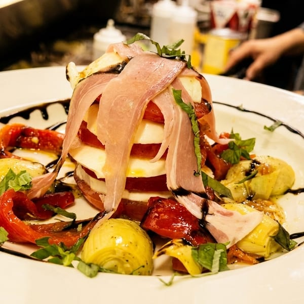 Caprese salad with prosciutto, mozzarella, tomatoes, roasted peppers, and artichoke hearts, drizzled with balsamic.