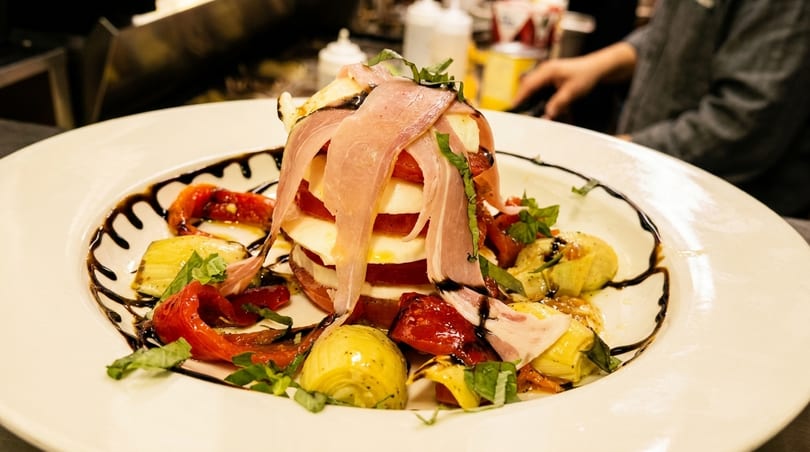 Caprese salad with prosciutto, mozzarella, tomatoes, roasted peppers, and artichoke hearts, drizzled with balsamic.