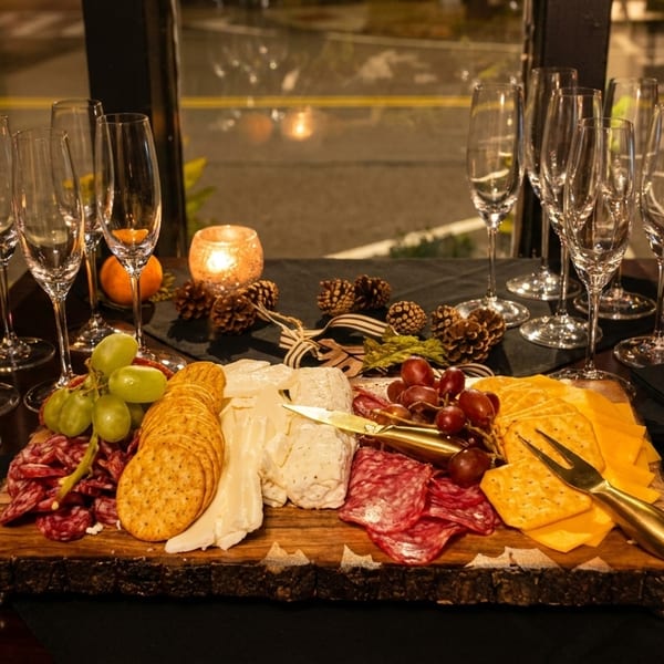 A charcuterie board with cheeses, meats, crackers, grapes, and champagne flutes on a dark table.