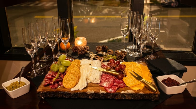 A charcuterie board with cheeses, meats, crackers, grapes, and champagne flutes on a dark table.