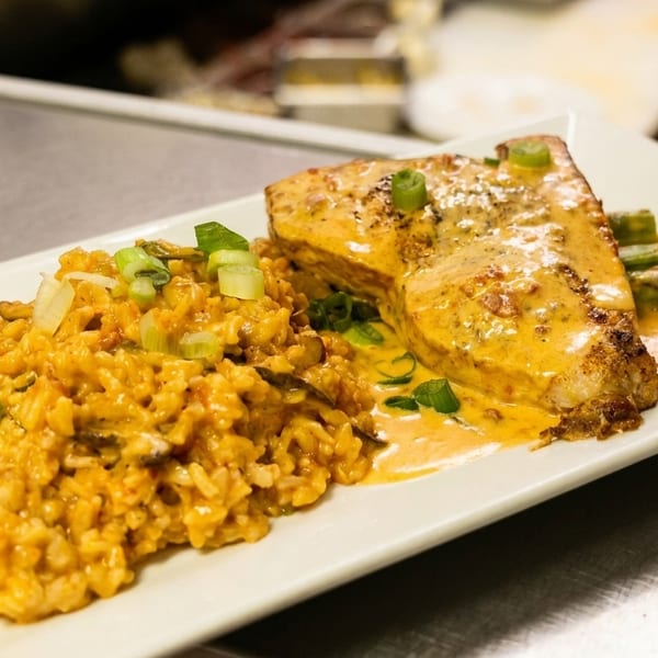 A plate of salmon with creamy sauce, risotto, and asparagus on a white rectangular plate.
